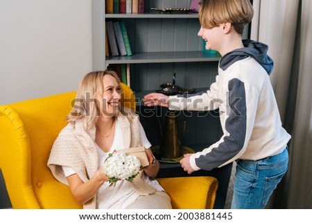 Portrait of smiling loving kid teen son hugging kissing happy young mom congratulating with mothers day. Cheerful young woman receiving gift from son. Concept of family holidays celebration.