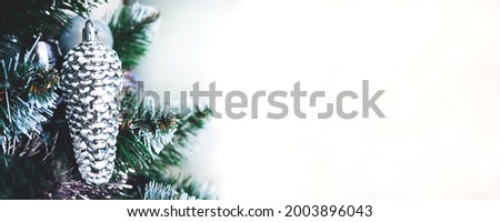 Silver white toy cone hanging on artificial Christmas tree on white background. Wide panoramic holiday banner with copy space
