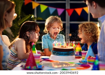 Kids birthday party. Child blowing candles on cake and opening presents. Pastel rainbow theme celebration. Family celebrating at home. Boy opening gifts, eating cakes. Sweets for children. Royalty-Free Stock Photo #2003940692