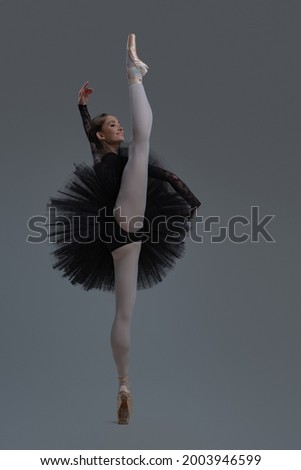 Agile ballerina in black dress against gray background
