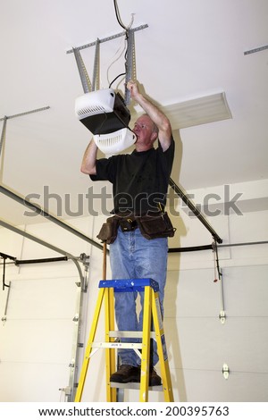 Man standing on a ladder fixing a mechanical garage door opener  Royalty-Free Stock Photo #200395763