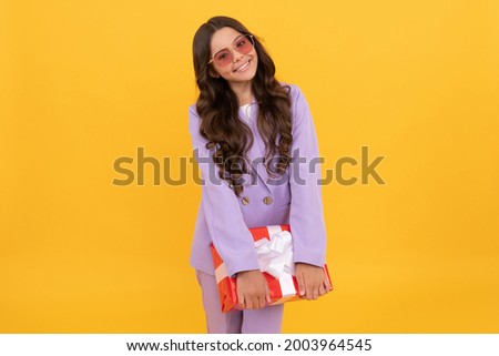 trendy cheerful child in sunglasses and suit hold present box on yellow background, happy birthday