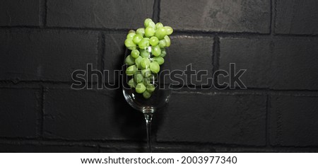 Picture of green grapes in the glass of wine, isolated on the black brick wall.
