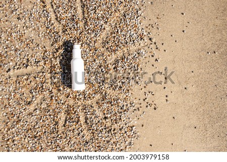The concept of sun protection, sunscreen, summer. The sun is drawn on the sea sand, in the middle there is a white liquid bottle of cream or lotion. Layout, place for text. Sunny day. Nobody. Mock up