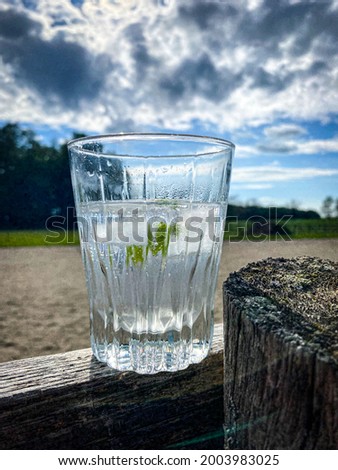 A refreshing glass of gin and tonic on a wooden fence post during summer time on a cloudy and hot summer day