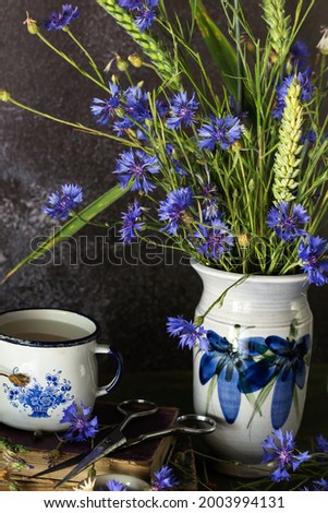 Bouquet of just cut cornflowers  with wheat plants in a vase on dark background, floral still life concept
