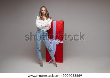 Pretty fit young girl with big red gift on gray studio background with copy space for holiday advertising