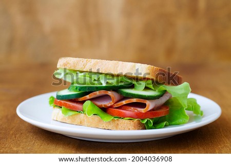 close up tasty sandwich with ham, green salad, cucumbers and tomatoes on the wooden background.toasted homemade sandwich with fresh vegetables on the white plate.copy space