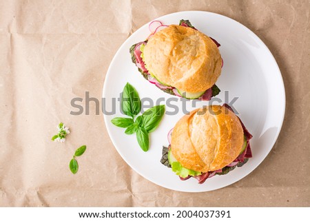 Ready-to-eat hamburgers with pastrami, vegetables and basil on a plate on craft paper. American fast food. Top view