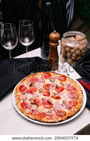 Meat pizza in Italian restaurant. High end food on white plate with wooden board and fresh ingredients. 