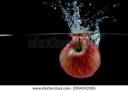 red apple fall into water with splashes on black background, place under text