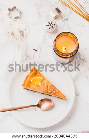 Christmas table. Plated slice of orange cheesecake on a table with festive Christmas decorations and scented candle. Copy space, top down view.
