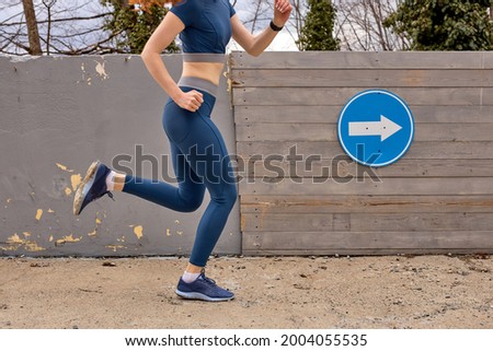 Healthy lifestyle. Fit woman have fitness day and running in urban area at daytime. Cropped female in blue sportive clothes runs fast forward, focused on training outdoors