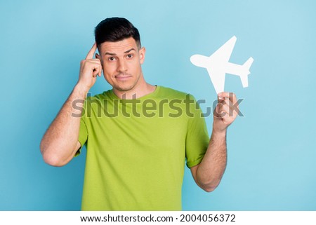 Photo portrait man in green t-shirt keeping paper plane thoughtful doubt isolated pastel blue color background
