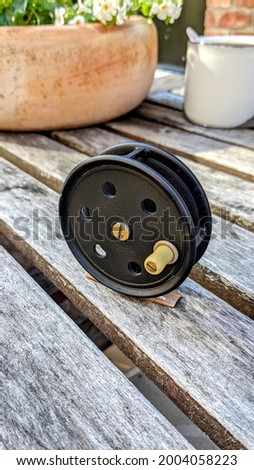 Vintage black fly reel on rustic wood with clay pot and flowers behind