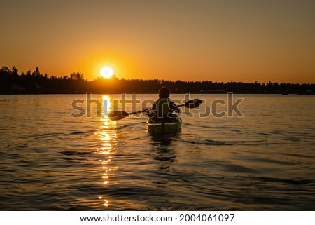 Girl kayaking and taking pause calm sea at midnight in Northern Sweden during light Summer nights. All day around Sun in polar regions. Royalty-Free Stock Photo #2004061097