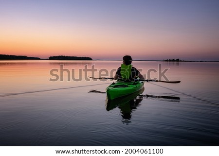 Kayaking women holding paddles horizontally, sea kayaking at midnight in Northern Sweden during light Summer nights. Mirror like water surface. Umea, Baltic Sea, Sweden Royalty-Free Stock Photo #2004061100