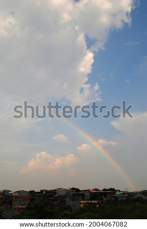 a beautiful rainbow appears in front of the cloudy blue sky above the settlement after rain