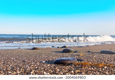 Photo from the shore between stones with waves in the sea and algae on the ground