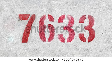 Red Number 7633 on the white wall. Spray paint. Number seven thousand six hundred thirty three.