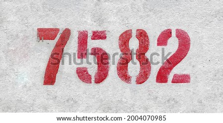 Red Number 7582 on the white wall. Spray paint. Number seven thousand five hundred and eighty two.