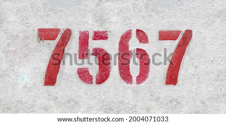 Red Number 7567 on the white wall. Spray paint. Number seven thousand five hundred and sixty seven.