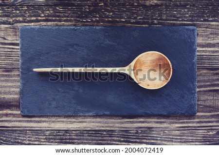 Old antique hand carved wooden spoon with deep bowl made of olive wood over a slate stone and rustic wood table background. Image shot from top view. Flatlay.
