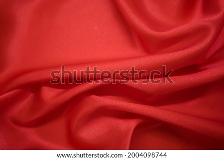 Abstract Red Satin Silky Cloth Fabric Textile Drape with Crease Wavy Folds background. With soft waves and, waving in the wind Texture of crumpled paper. Background texture, pattern. Red silk fabric