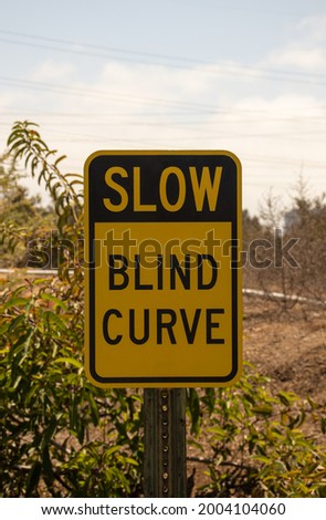 A Slow Blind Curve sign on the road.