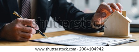 Real estate agent holding home and signing a contract about the agreement of real property on desk, businessman writing on document form rent house, broker and planning investment, business concept.