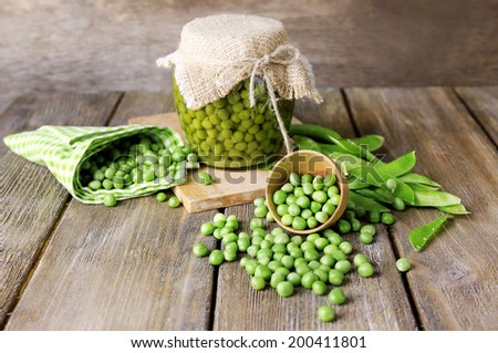 Fresh  and canned peas in bowl and glass jar on napkin, on wooden background