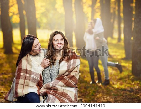 Two young best girlfriends covered in blanket while their friends having photo session