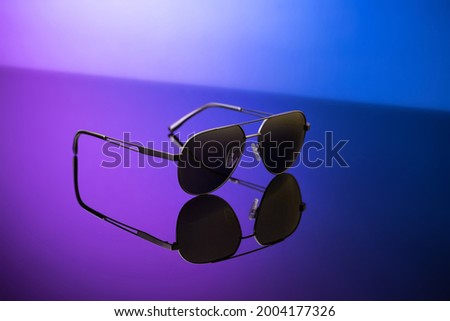 Black sunglasses on blue reflective surface, closeup. Product photography and fashion concept