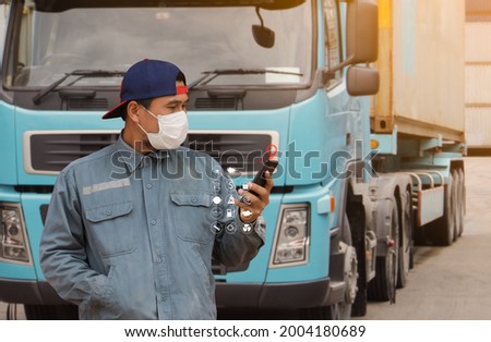 man truck driver transport wearing a medical mask Finds a location on his smartphone digital icon display. background semi-truck container delivery warehouse