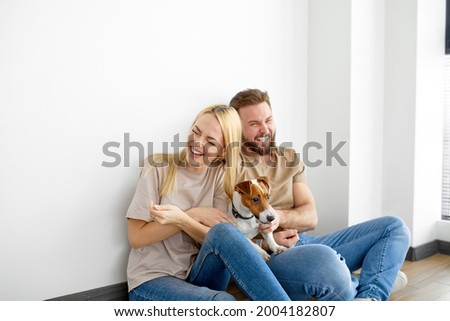 Cheerful caucasian couple family sit on floor playing with pet dog, have fun, enjoy weekends together, laugh, in casual outfit, talking. Harmonious relationships, family, spare time, free time concept Royalty-Free Stock Photo #2004182807