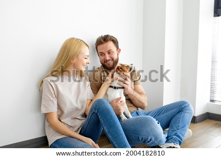 Couple With Dog At Home, Having Fun, Enjoy Spending Time Together, Side View Portrait. Handsome Bearded Guy And Blonde Female Laugh, Holiday At Home. In Bright Cozy Room. People Lifestyle Concept