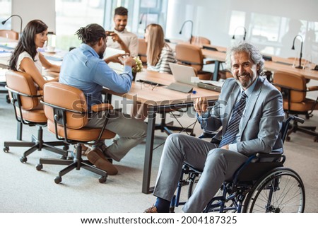 Portrait of smiling disabled business executive in wheelchair at meeting. Paralyzed man in a wheelchair. Shot of a team of businesspeople having a meeting in a modern office. 