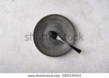 Empty plate and spoon. Dark kitchen utensils set on light gray table. Top view flat lay with copy space