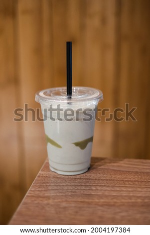 A cup of smoothie with black plastic straw on the edge of a wooden table with wooden textured background