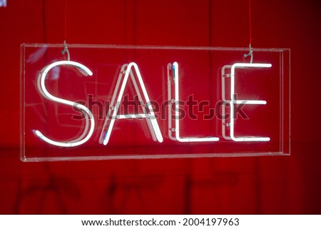 Neon sale sign sparkling in a red shop-window, sales season, promotion