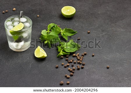 Glass of refreshing drink with lime, mint and ice. Lime slices and mint leaves on table. Copy space. Black background. Top view
