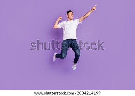 Full length photo of happy young cheerful man jump up point finger empty space isolated on purple color background