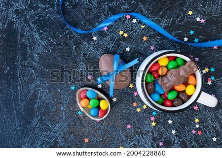 various chocolate candies in white mug on black texture background. egg-shaped sweets and chocolate rabbit. top view flat lay. soft focus