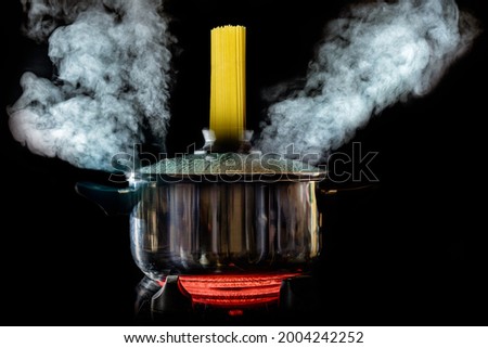 Concept photo of cooking spaghetti in stainless steel pot with steam water vapor exiting the pot and spaghetti entering the pot against a black background.