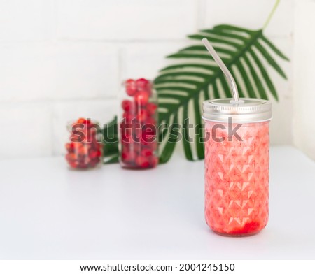 still life with a bottle of berry smoothie, berries in jars, and a branch of palm