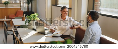 Female discussing new project with male colleague. Mature woman talking with young man in office. Royalty-Free Stock Photo #2004245780