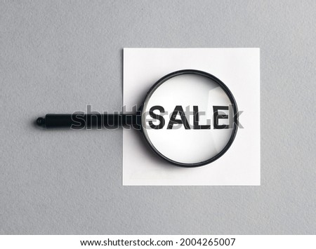 Sale word on paper through magnifying glass on gray background.