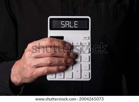 Sale word on calculator in businessman hand on black background.