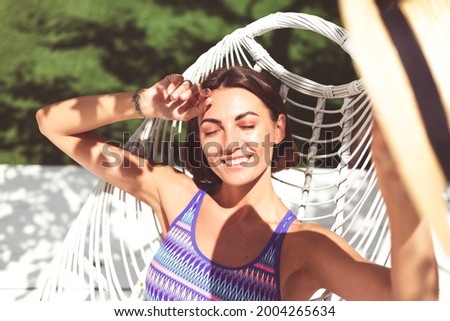Beautiful woman sit on backyard chair at summer sunny day enjoying amazing warm weather, catching sun rays, cheerful happy