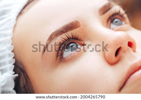 Young woman with beautiful eyebrows after procedure permanent make-up in salon, closeup photo.